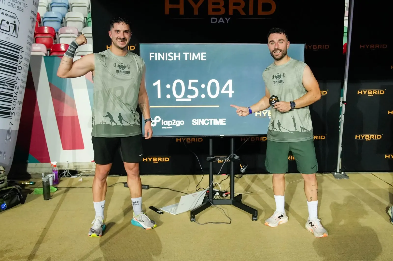 Dois atletas do M2 ao lado do ecrã com o tempo final de 1:05:04 no Hybrid Day