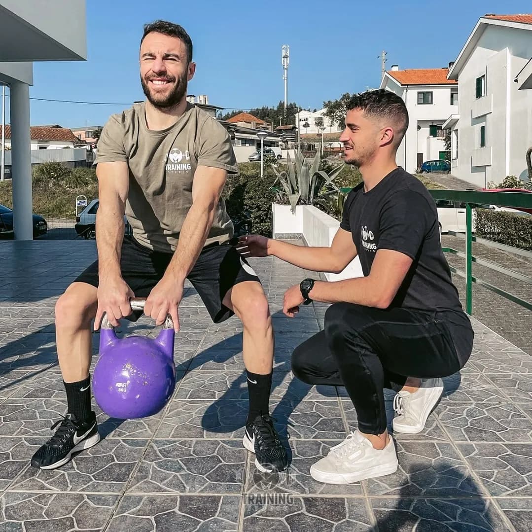 PT a corrigir a postura de um cliente num exercício com kettlebell, no exterior